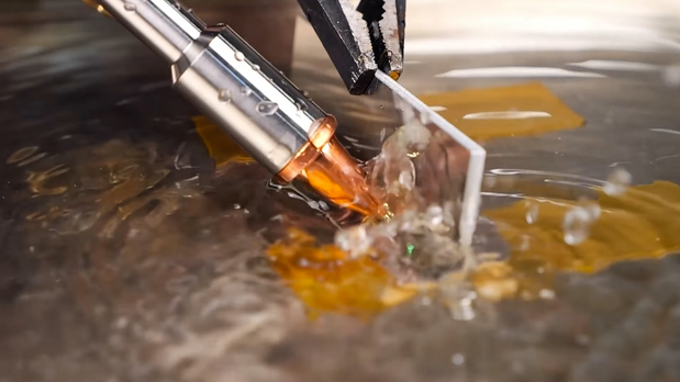 Close-up of an X1 Pro laser welding nozzle working on a metal T-joint submerged in shallow water